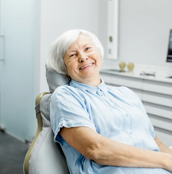 Smiling senior woman with white hair sitting comfortably in a dental chair at a dental office.